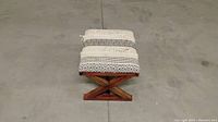 Solid wooden stool with fabric cushion top resting on a concrete floor.