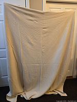 Full view of beige 100% cotton blanket held up showing size and texture