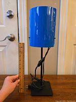 Blue Ikea table lamp with cylindrical shade, black stem and base, held next to a ruler to show height approximately 13 inches.
