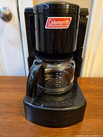 Black Coleman drip coffeemaker with glass carafe showing branding and measurement markings.