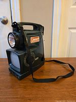 Full view of vintage Coleman multi-functional lantern with TV screen and flashlight, showing carrying handle and shoulder strap.