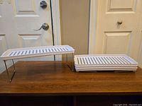 Four white plastic folding cabinet shelves, one set up with metal legs extended, three folded flat on table