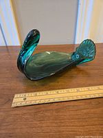 Green glass swan-shaped candy dish on a wooden surface with ruler for size reference.