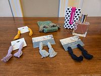 Photo showing five pairs of handmade macrame tassel earrings in yellow, lavender, grey, black, and olive green, displayed on a wooden surface beside the Romantic perfume bottle and packaging.