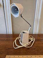 Front view of the mid century modern desk lamp on a wooden surface, showing hexagonal base, adjustable arm, and the inner reflective shade and light bulb.