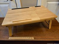 Front view of the bamboo lap tray showing foldable legs and horizontal flat surface with device holding slots.