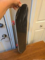 Side view of the sealed skateboard showing black grip tape and red wheels.