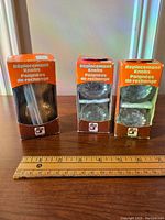 Three vintage replacement door knobs in original orange and brown packaging, set side by side with a ruler in front for scale.