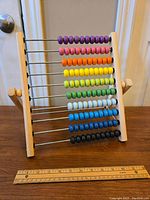 Wooden abacus with all beads aligned on the left, placed upright next to a 12-inch ruler for scale.