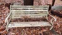 Front view of weathered wooden slat bench with cast iron sides sitting on the ground covered with brown autumn leaves.