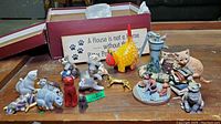 Wide view of cat figurines collection including colorful cats, Lladro piece, and decorative sign with paw prints.