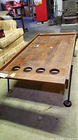 Full view of the vintage wood coffee table showing its rectangular shape, metal legs and five circular holes on one side, with visible surface damage.