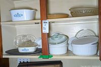 Shelf display showing various Corningware casseroles including two with blue cornflower pattern, clear glass pie plates, and white bakeware dishes.