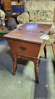 Full front view of the vintage wooden dough box style end table showing hinged top, carved legs, and metal handle on side.