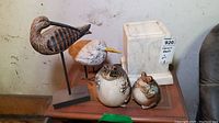 Lot overview showing two wooden bird figurines, two ceramic frogs, and a white marble-like pedestal on a wooden table.