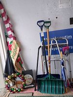 Photo showing walker, two green-handled snow shovels with wooden handles, multiple canes, a blue and white striped umbrella, holiday candy cane decoration, wooden decorative signs, jingle bell wreath with metallic bells, and a folded American flag