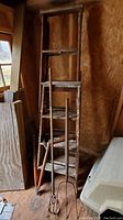 Two views of the same corner showing two weathered wooden ladders leaning against a plywood wall inside a shed. The larger ladder is about 6ft and the smaller about 4ft. The ladders have chipped paint and are rustic in appearance.