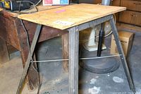 Side view showing angled metal legs and bracing wire underneath a plywood work surface with signs of wear.