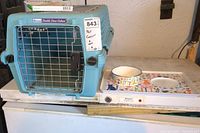 Front angle view showing the blue pet carrier with metal grid door and the rectangular magnetic feeding tray with a single removable cat bowl.