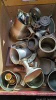Photo showing various pewter vessels including pitchers, cups, goblets, salt and pepper shakers, and bells inside a box.
