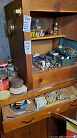 Overview of wooden cabinet with plumbing supplies on shelves and in drawers, including metal and plastic fittings, tools, and containers.