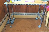 Full view of the rolling desk with wooden top, metal wire lower shelf, and castors.