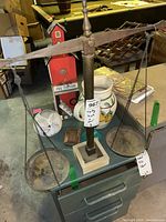 Vintage balance scale with iron pans hanging on chains and square stone base displayed on metal filing drawers in basement setting.