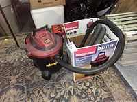 Full view of the 5 gallon Shop Vac unit showing attached hose, vacuum body in black and red, surrounded by original packaging box and accessories inside the box.
