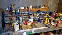 Wide view of blue steel shelving units labeled 'Fastener Center' containing multiple small drawers and numerous jars, boxes, and tins of assorted screws, nails, nuts, bolts, and other small hardware on a grey workbench.