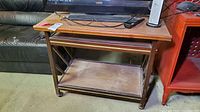 Front view of vintage wooden rolling TV stand with added platform shelf needing cleaning.