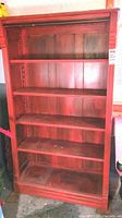 Full front view of red-painted wooden bookcase showing four adjustable shelves and plank back panel.