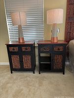 Two wood side tables with wicker drawer and door panels, both with matching lamps on top.