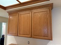 Front view of closed 3 door oak upper cabinet with crown molding along the top edge.