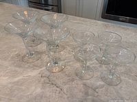 Eight clear glass stemmed martini glasses shown on countertop, including a mix of styles.