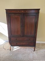 Front view of antique country style armoire showing closed two panel doors and two drawers below.