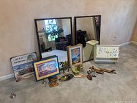 Wide view showing two large framed mirrors, framed beach-themed artworks, small accessory items including soap dispensers, toothbrush holders, decorative pieces, and metal door hooks on carpet.
