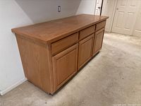 Front and side view of oak lower cabinet showing three drawers on top and three doors below, placed against wall on carpet.