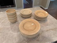 Ceramic dinnerware set arranged on countertop showing stacked plates and bowls grouped by type.