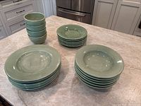 All pieces of the set including stacked bowls, salad plates, dinner plates, and the large platter on a kitchen countertop.