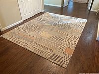 Full view of the rectangular cream background rug with geometric patterns on hardwood floor.