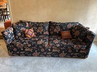 Front view of a black sofa with a floral print upholstery and four pillows, two matching the sofa fabric and two smaller colorful accent pillows.