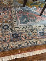 Close-up view of the rug border pattern and white fringe showing detailed design and colors of blue, rust, beige, and gold.