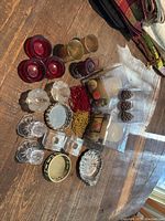 Top-down photo showing an assortment of candle holders, candle bases, two sets of votive holders, and beaded wine bottle covers arranged on a wooden surface.