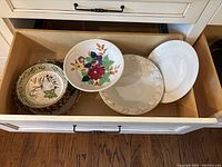 Drawer open showing six ceramic pasta serving sets and bowls; three bowls on top with floral and vine patterns, three ceramic plates underneath with embossed and painted decorations.
