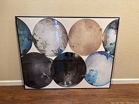 Full image of framed contemporary art showing seven circular abstract shapes in blue, beige, black, white, and gray.