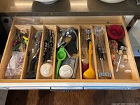 Full kitchen utensil drawer showing multiple segregated compartments with a variety of utensils including can openers, measuring spoons, citrus juicers, and scissors.