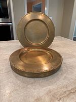 Stack of brass chargers showing their shape and decorative beaded rim detail.