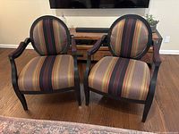 Front view of two Queen Anne style chairs with round backs and striped multicolor upholstery placed on wooden floor.