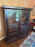 Front view of the dark brown wooden cabinet with leaded glass doors and bottom drawers