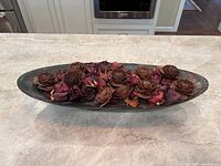 Top view showing the elongated oval raku ceramic vase filled with dried roses and pine cones arranged evenly across the surface.